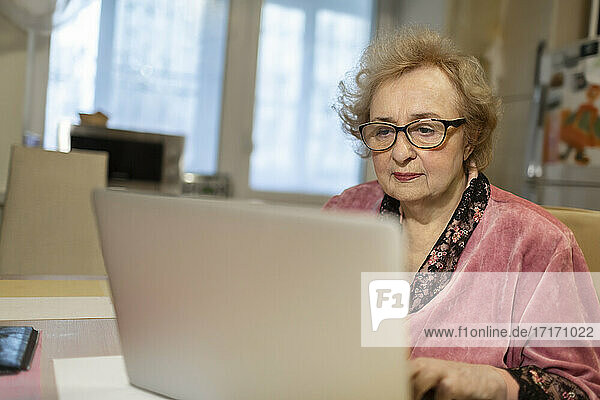 Ältere Frau mit Brille benutzt Laptop im Wohnzimmer