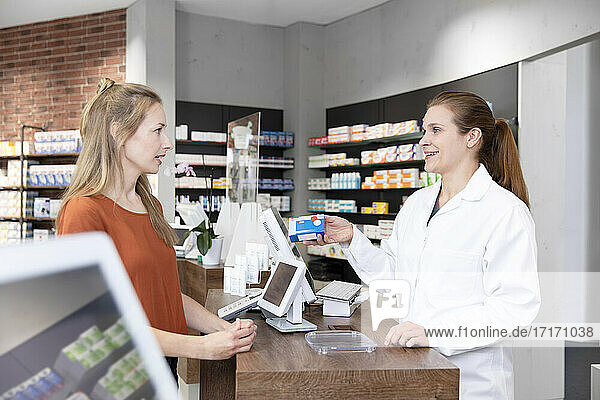 Female pharmacist advising medicine prescription to woman at checkout in store