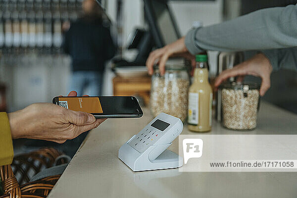 Älterer Kunde mit Mobiltelefon beim Bezahlen mit Barcode-Scanner in einem Einzelhandelsgeschäft