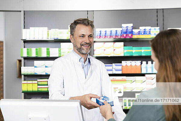 Smiling man giving medical prescription to female customer at pharmacy checkout