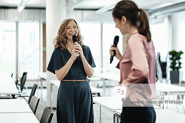 Weibliche Kollegen singen lächelnd durch das Mikrofon während der Pause im Büro