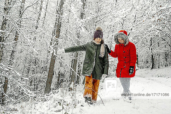 Teenage girl with sister walking on snow in forest during winter