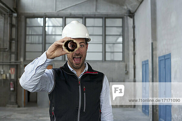 Männlicher Architekt mit offenem Mund  der durch einen Karton schaut  während er in einem Gebäude steht