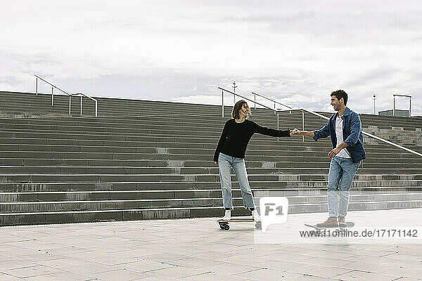 Young couple skateboarding walking near steps