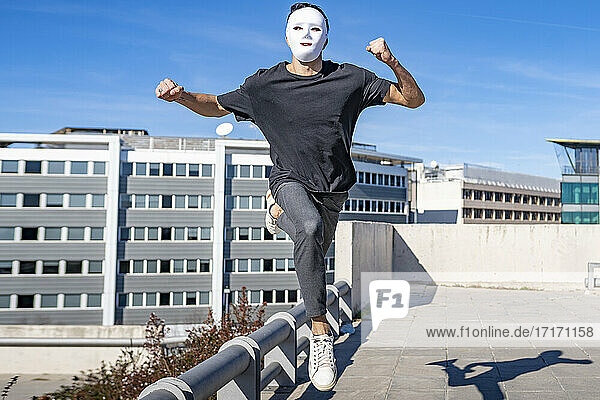 Man wearing mask running on rooftop during sunny day