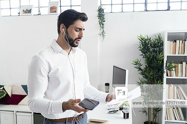 Young male entrepreneur discussing over pie chart through smart phone while working in office