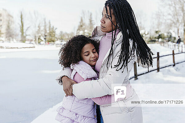 Tochter  die ihre Mutter umarmt  während sie im Schnee im Park steht