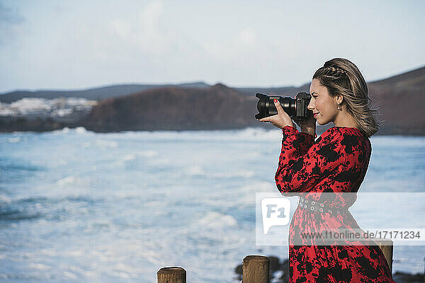 Junge Frau beim Fotografieren mit der Kamera  während sie am Meer steht  in El Golfo  Lanzarote  Spanien