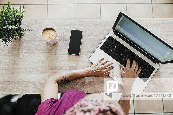 Unternehmerin bei der Arbeit am Laptop mit Smartphone und Kaffeetasse zu Hause