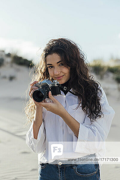 Beautiful young woman with vintage camera standing against sky