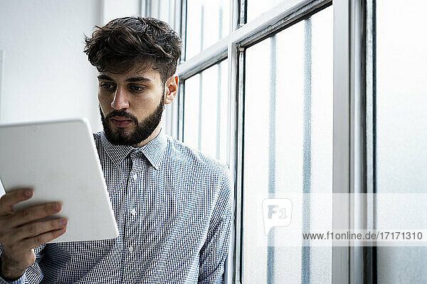 Young businessman using digital tablet by window in creative office