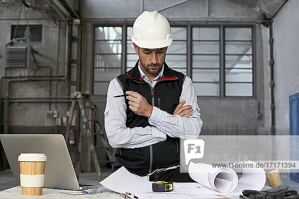 Männlicher Ingenieur beim Analysieren eines Bauplans auf einem Tisch in einem Gebäude
