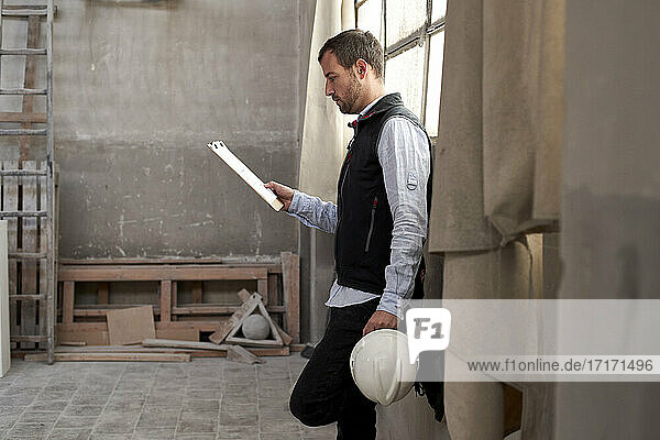 Männlicher Bauunternehmer analysiert ein Dokument  während er im Gebäude steht