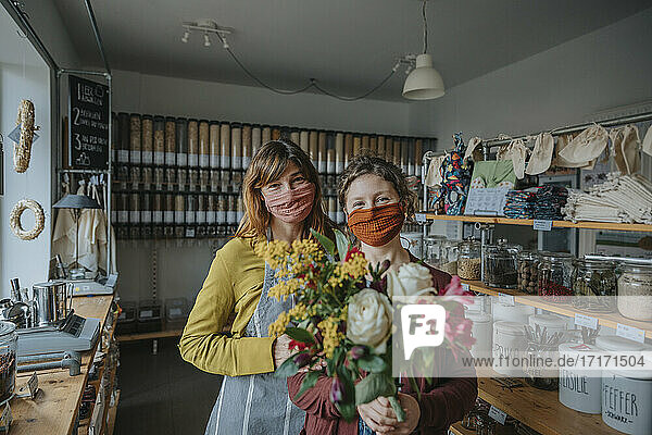 Unternehmerin mit Angestellter  die einen Blumenstrauß hält  während sie in einem Einzelhandelsgeschäft während einer Pandemie steht