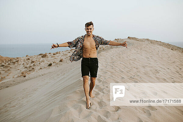 Cheerful young man doing shaka sign while walking on sand dunes at Almeria  Tabernas desert  Spain
