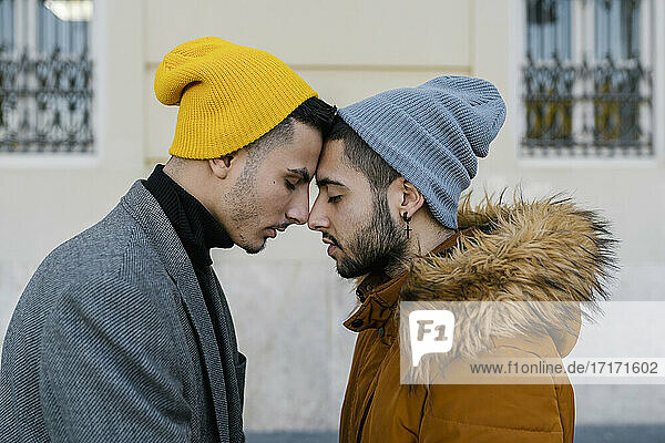 Homosexuelles Paar mit Strickmütze  das sich mit geschlossenen Augen an der Wand gegenübersteht