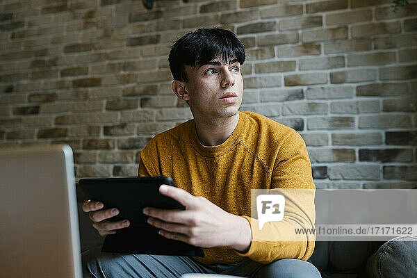 Mann mit Laptop und digitalem Tablet  der in einem Café sitzt und wegschaut