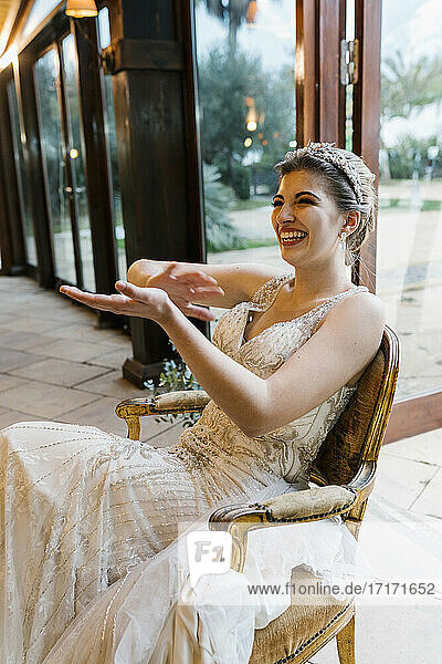 Happy bride clapping hands while sitting on chair at banquet