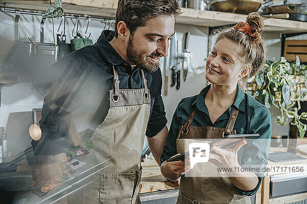 Smiling chef using digital tablet while standing by colleague in kitchen