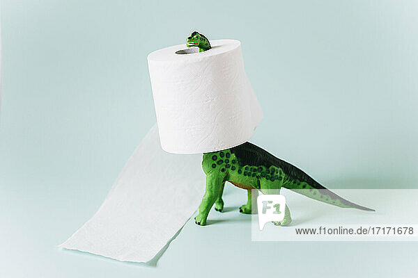 Diplodocus Dinosaurier Spielzeug mit einer Rolle Toilettenpapier um den Hals auf mintgrünem Hintergrund