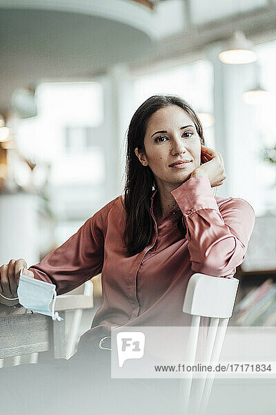 Female entrepreneur with hand on chin sitting in cafe during pandemic