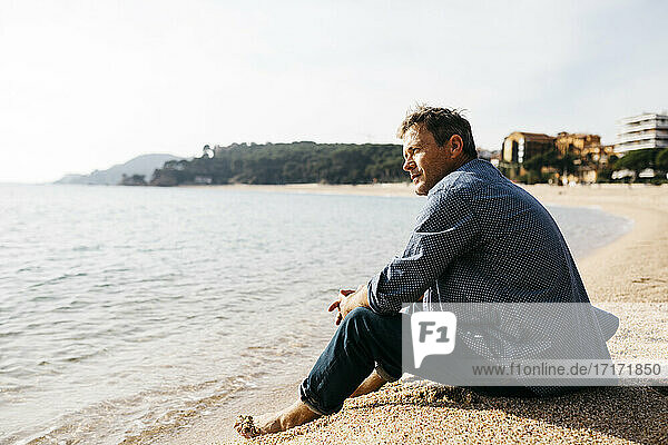 Mann sitzt am Strand auf Sand am Rande des Wassers an einem sonnigen Tag