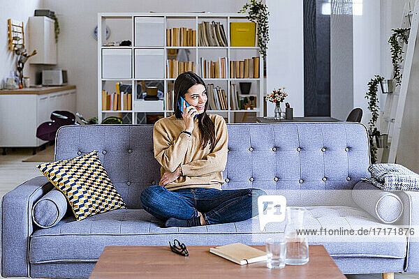 Smiling woman talking on mobile phone while sitting on sofa at home
