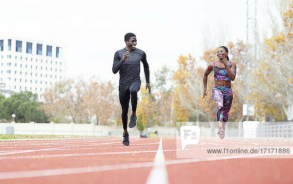 Happy male and female athlete running on track against clear sky
