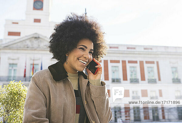 Smiling woman talking on mobile phone while standing in city