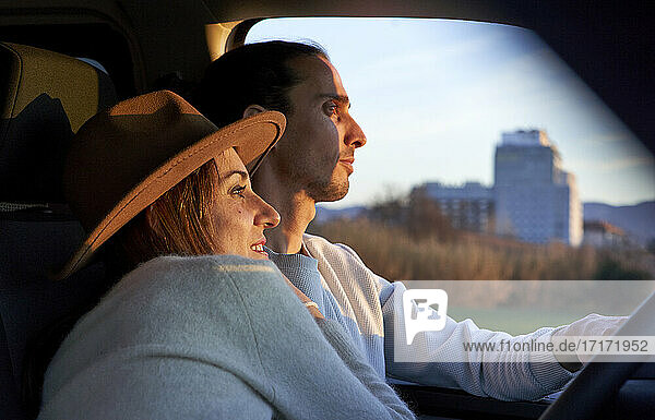 Man driving car while female embracing during sunset