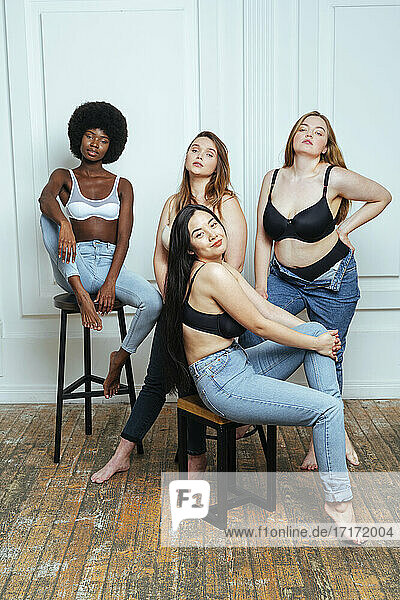 Confident multi-ethnic group of women in bras and jeans posing against wall