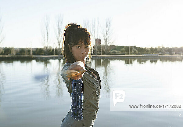 Selbstbewusste weibliche Kampfsportlerin hält ein Schwert  während sie an einem sonnigen Tag am See steht