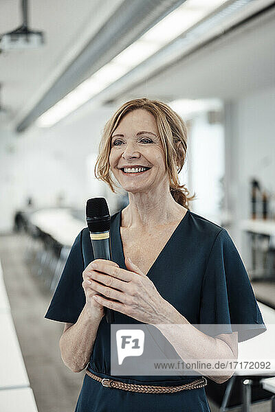Lächelnde Geschäftsfrau mit Mikrofon im Sitzungssaal eines Büros