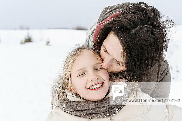 Close-up of mother kissing smiling daughter during winter
