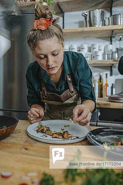 Young female chef garnishing dish while standing in kitchen