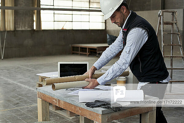 Männlicher Architekt legt Baupläne auf einen Tisch in einem Gebäude auf einer Baustelle