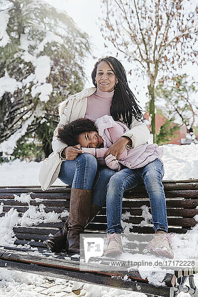 Tochter ruht den Kopf auf dem Schoß der Mutter  während sie im Winter auf einer Bank im Park sitzt