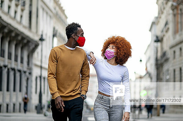 Young woman wearing protective face mask looking at man while walking in city