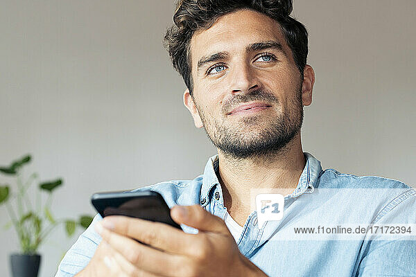 Mann mit blauen Augen  der wegschaut  während er zu Hause ein Mobiltelefon benutzt