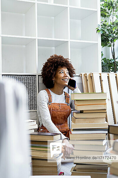 Afro-Frau am Telefon  umgeben von einem Stapel Bücher beim Umzug in eine neue Wohnung