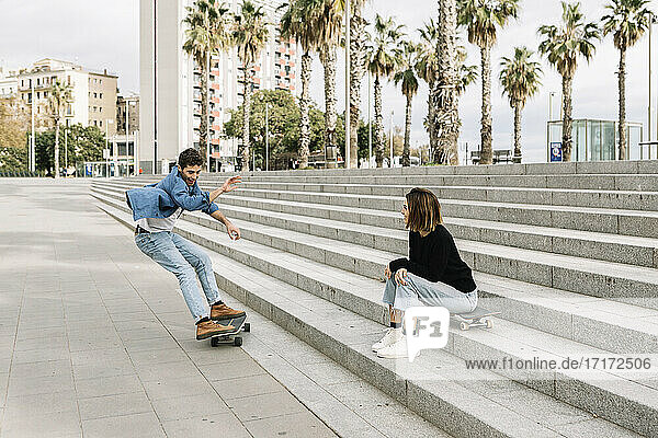 Young woman sitting on steps  looking at man skateboarding