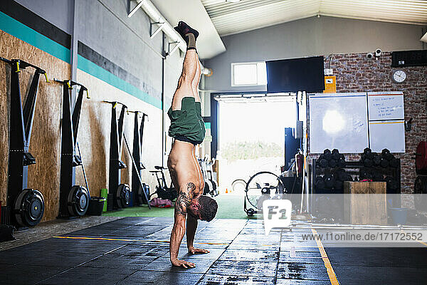 Shirtless male athlete practicing handstand on floor in health club