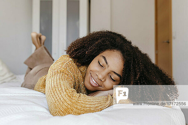 Junge Frau lächelt  während sie zu Hause auf dem Bett liegt