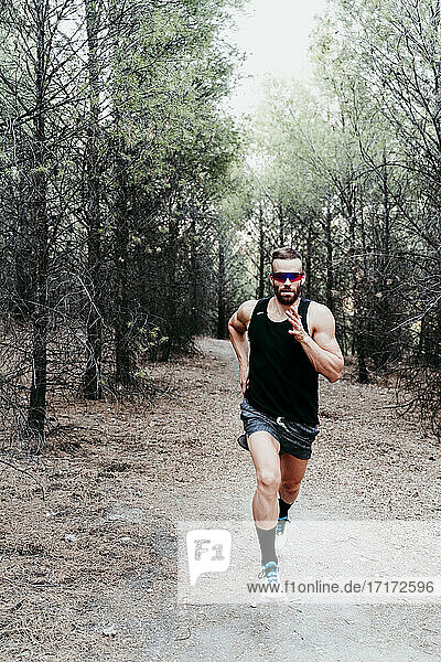 Handsome male athlete running on mountain trail in forest
