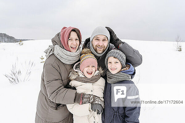 Glückliche Familie auf schneebedecktem Land gegen den Himmel im Urlaub stehend