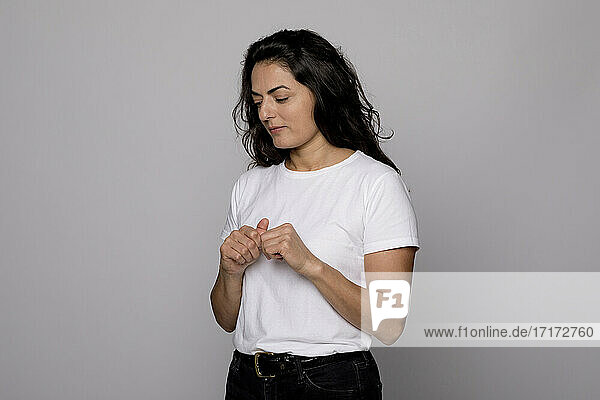 Thoughtful woman in white T-shirt standing against gray background