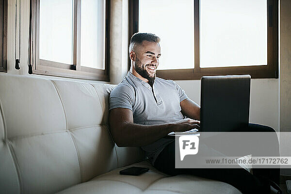Smiling businessman working on laptop while sitting on sofa at home
