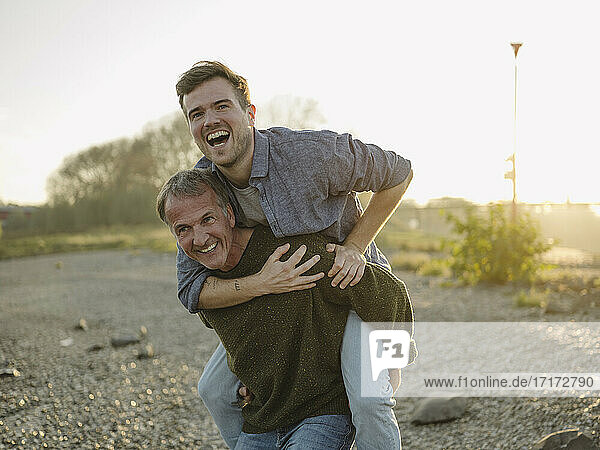 Cheerful father carrying son piggyback at riverbank