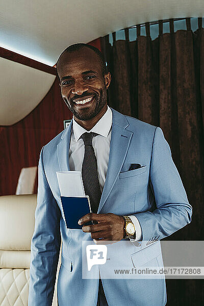 Happy businessman with passport standing in private jet