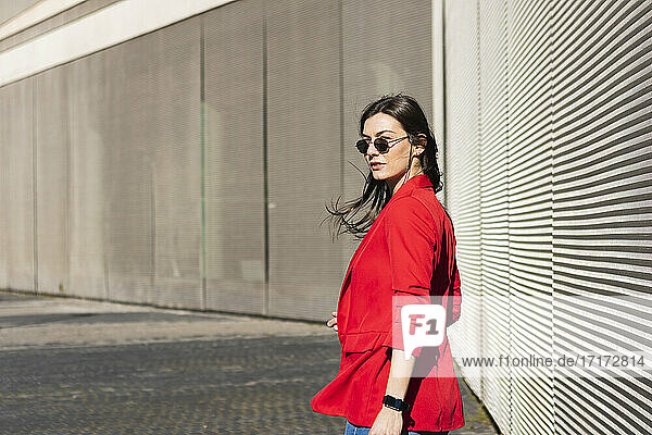 Businesswoman with sunglasses looking away while standing against wall